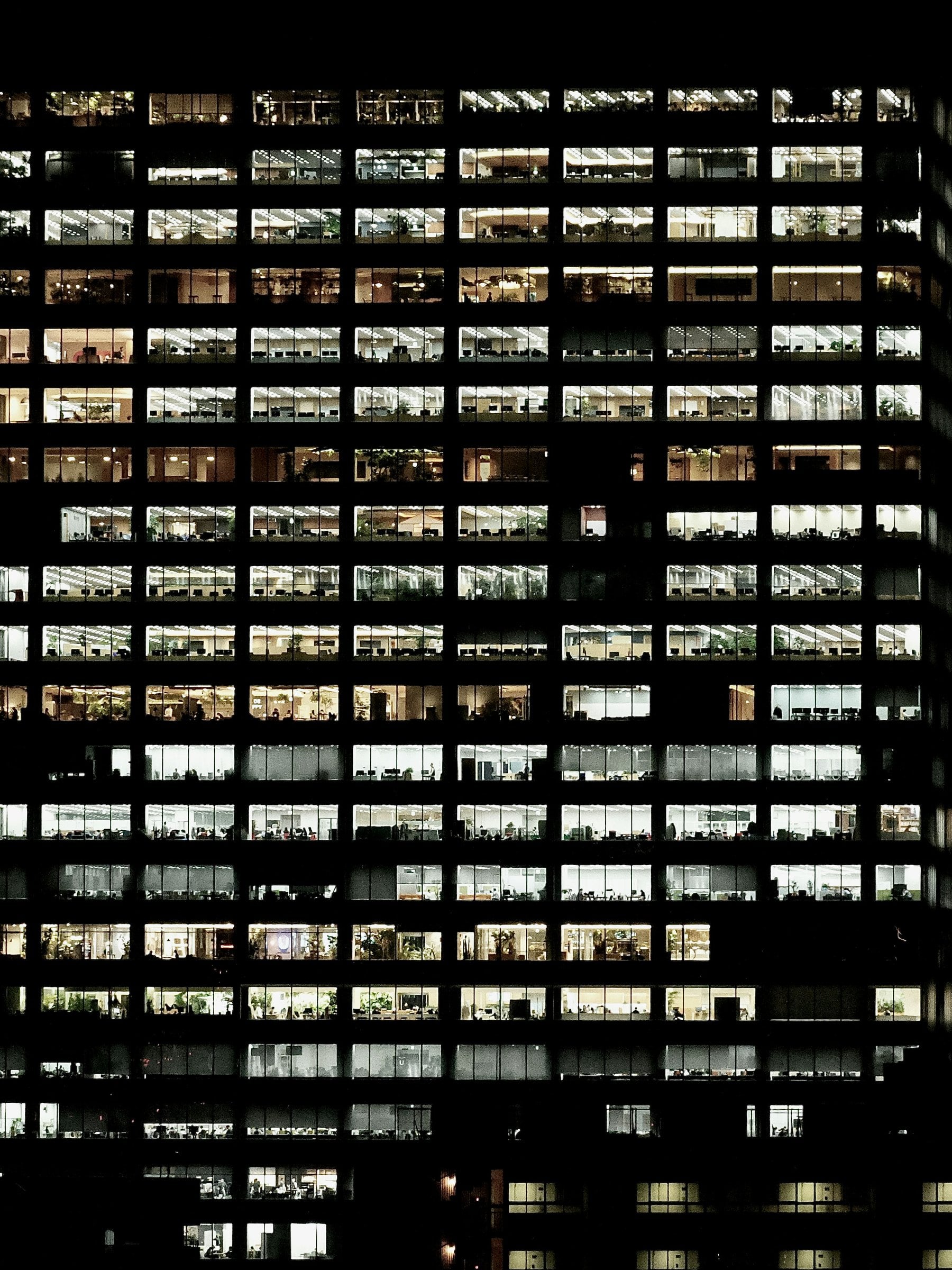 夜のオフィスビルの窓に灯りが並ぶ写真