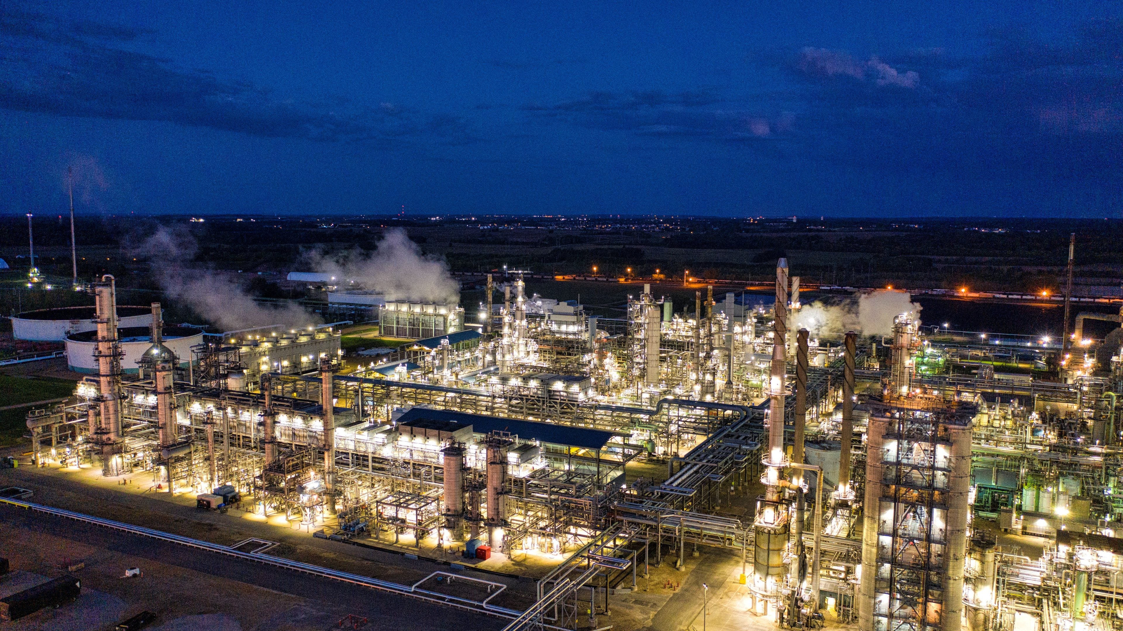 An aerial view of a petrochemical plant at night, its towers and piping lit in gold